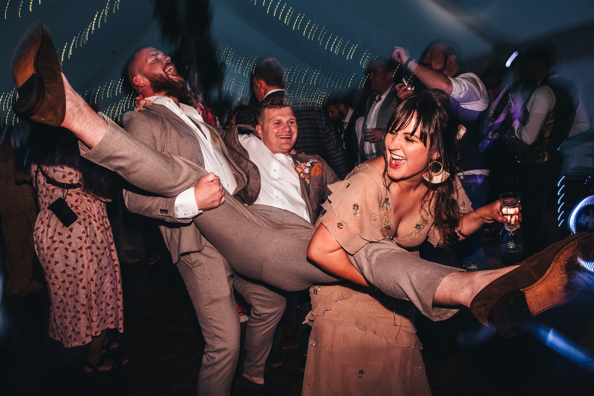 two people hold up groom on dancefloor