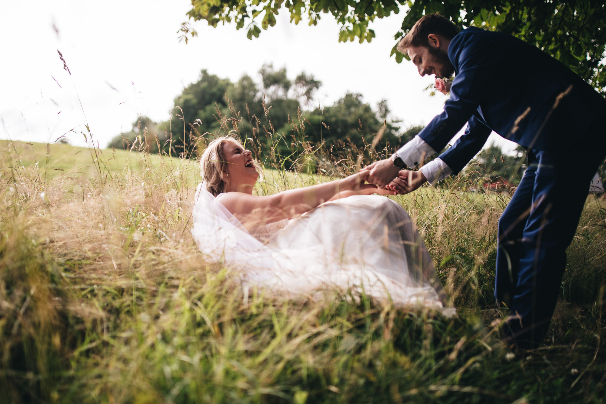 groom helps bride up out of the grass on the floor