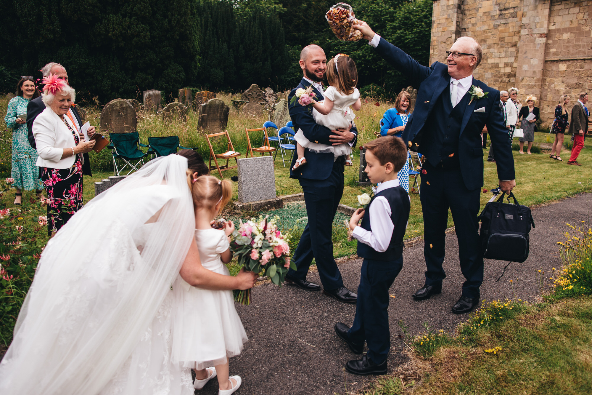 groom holds child dad throws confetti and bride hugs flower girl