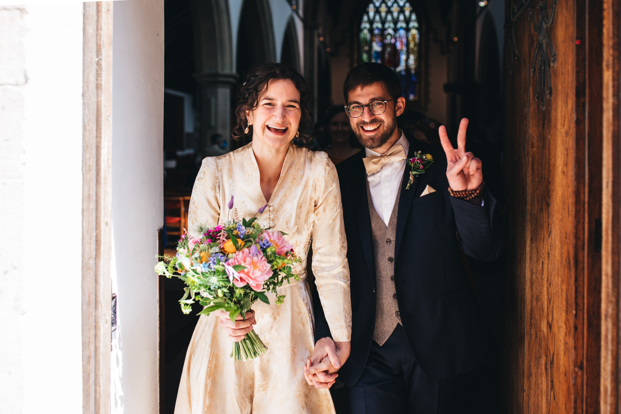 groom gestures peace symbol as the couple leave the church