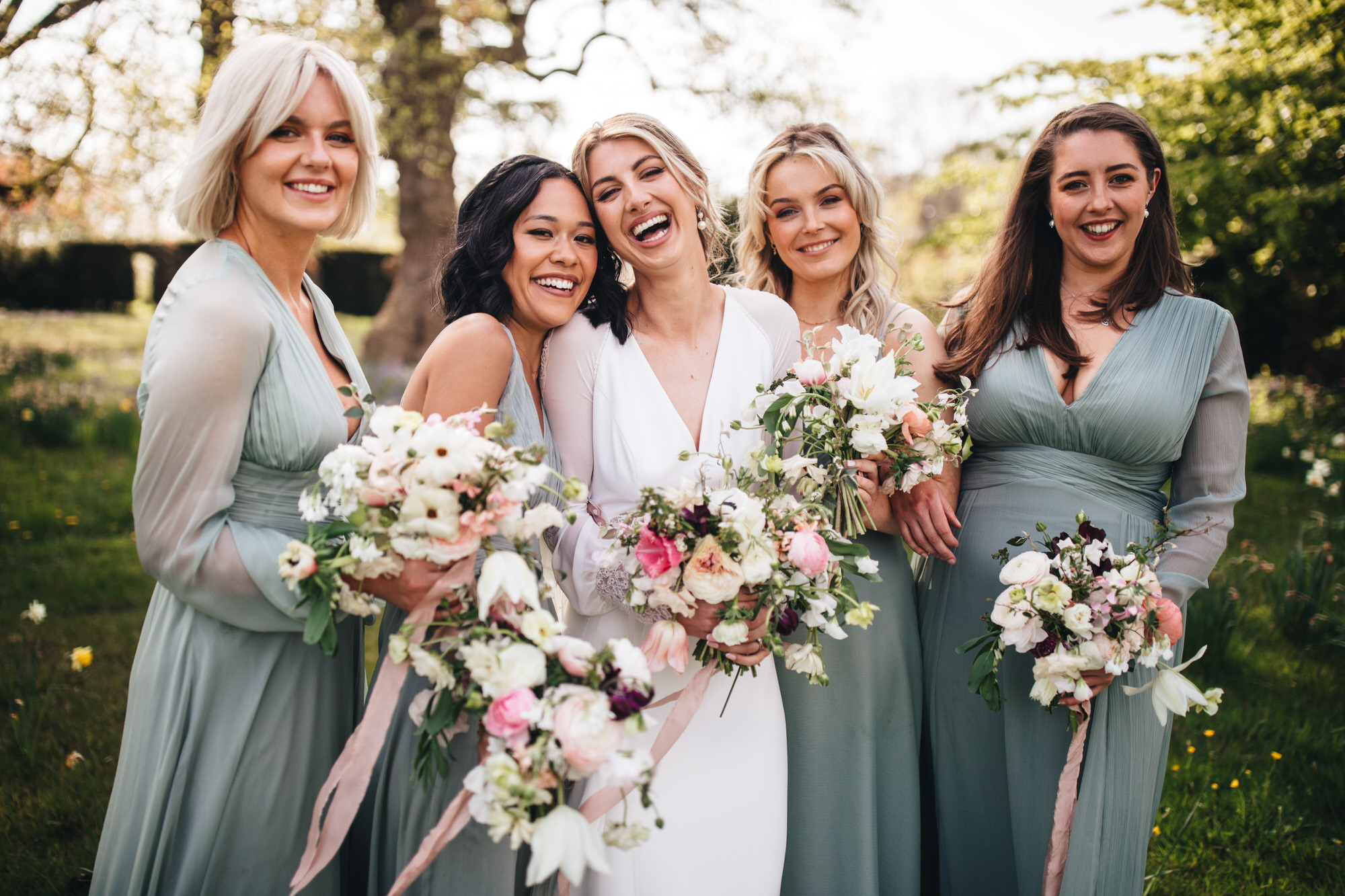 bride and bridesmaid under tress in gorgeous light laughing and holding their wedding bouquets
