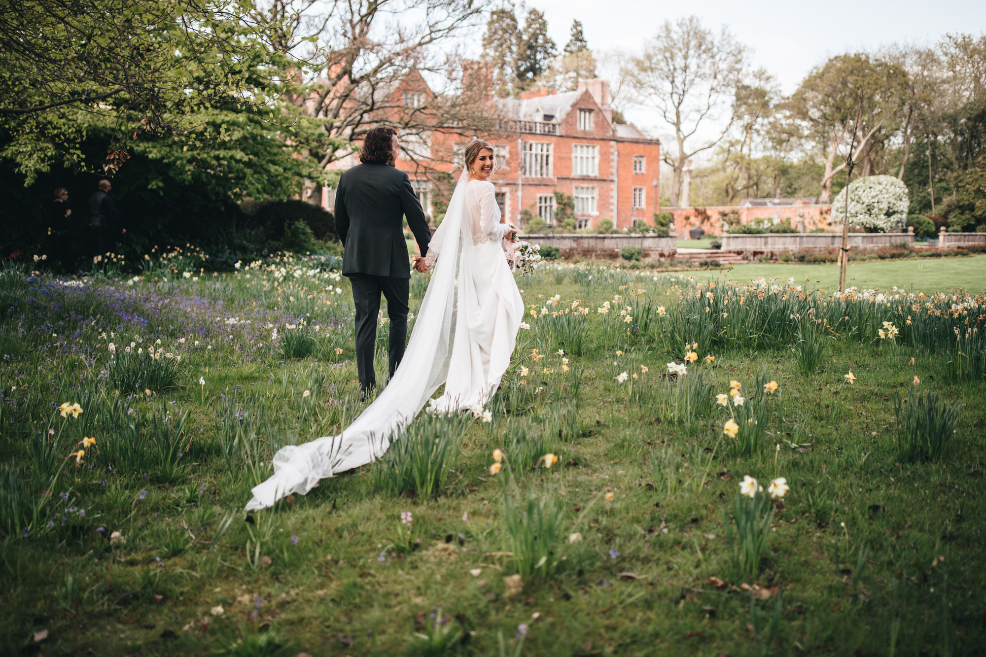spring flowers on grass floor under trees as couple walk away