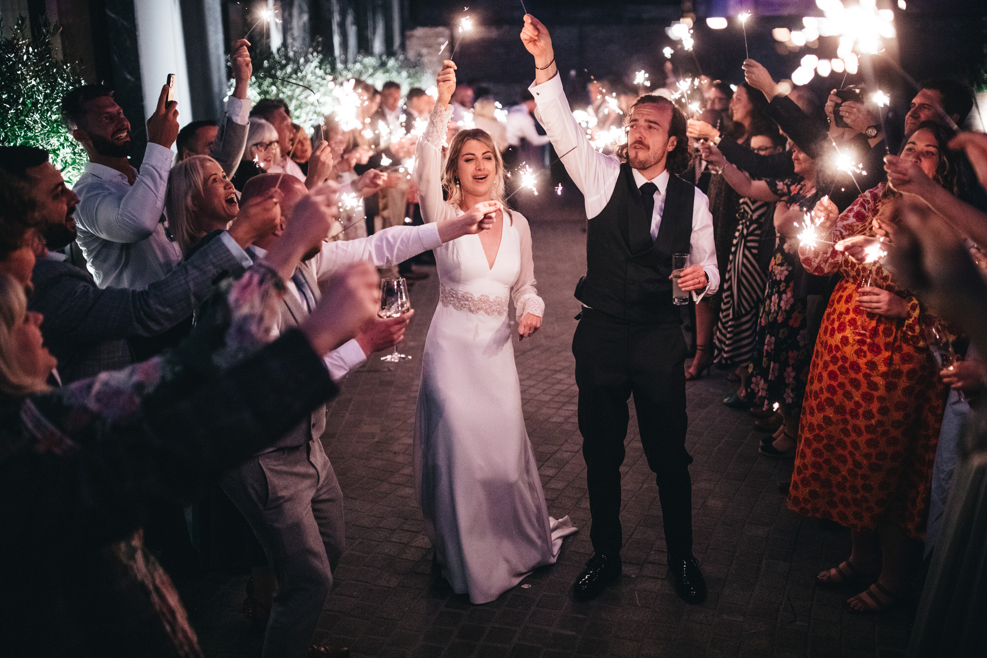 newly wed married couple holding sparklers above their heads with guests to celebrate wedding photography