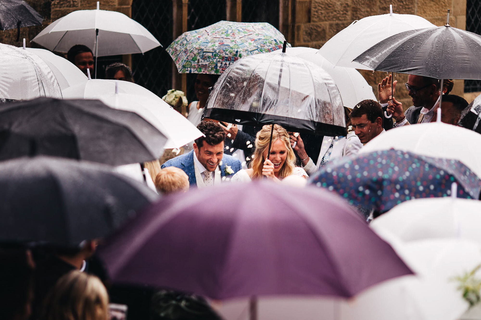 couple under umbrellas in rain at wedding
