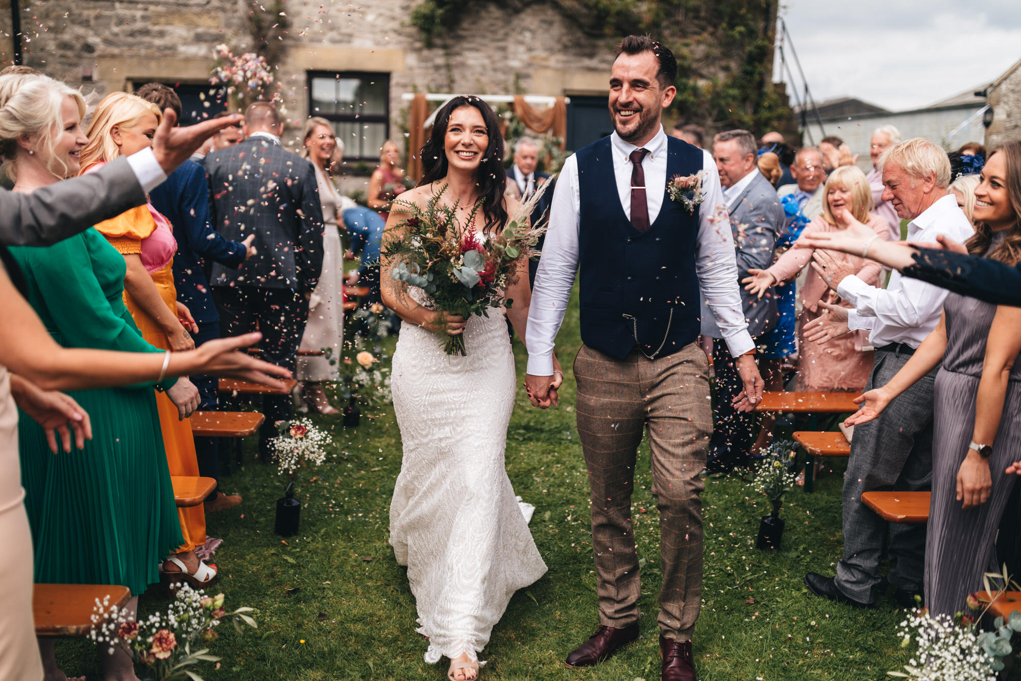 guests throw confetti at couple as they walk back down the aisle married