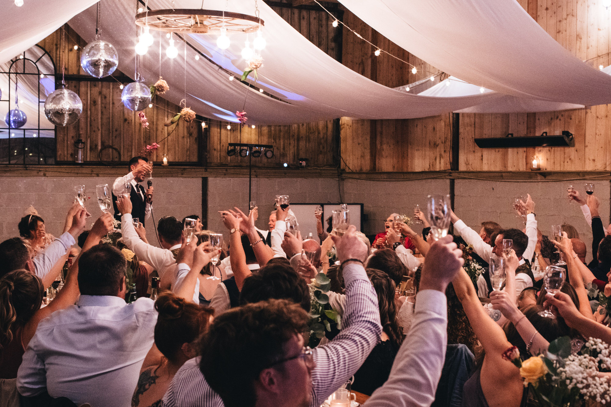 all guests raise a glass to toast married couple in wedding barn