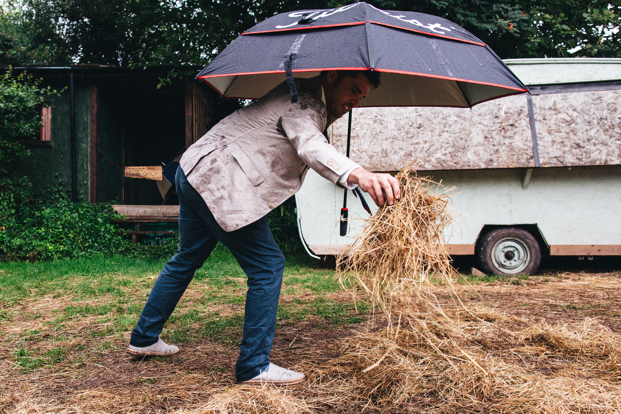 man spreading hay on grounds in rain