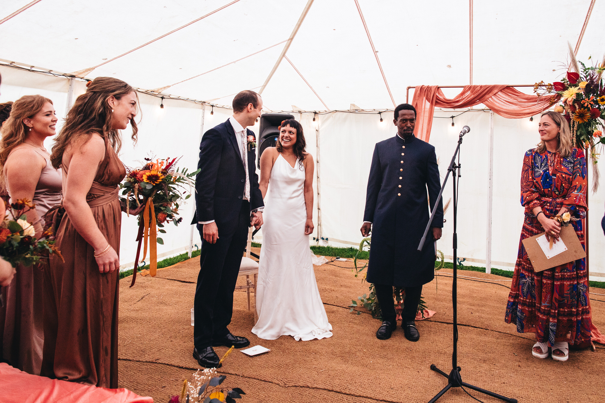 bride laughing at groom inside marquee with celebrant and bridesmaids
