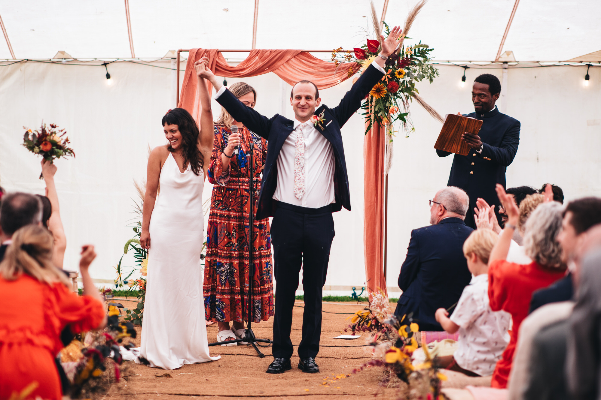 bride and groom married holding hands in air while guests are clapping