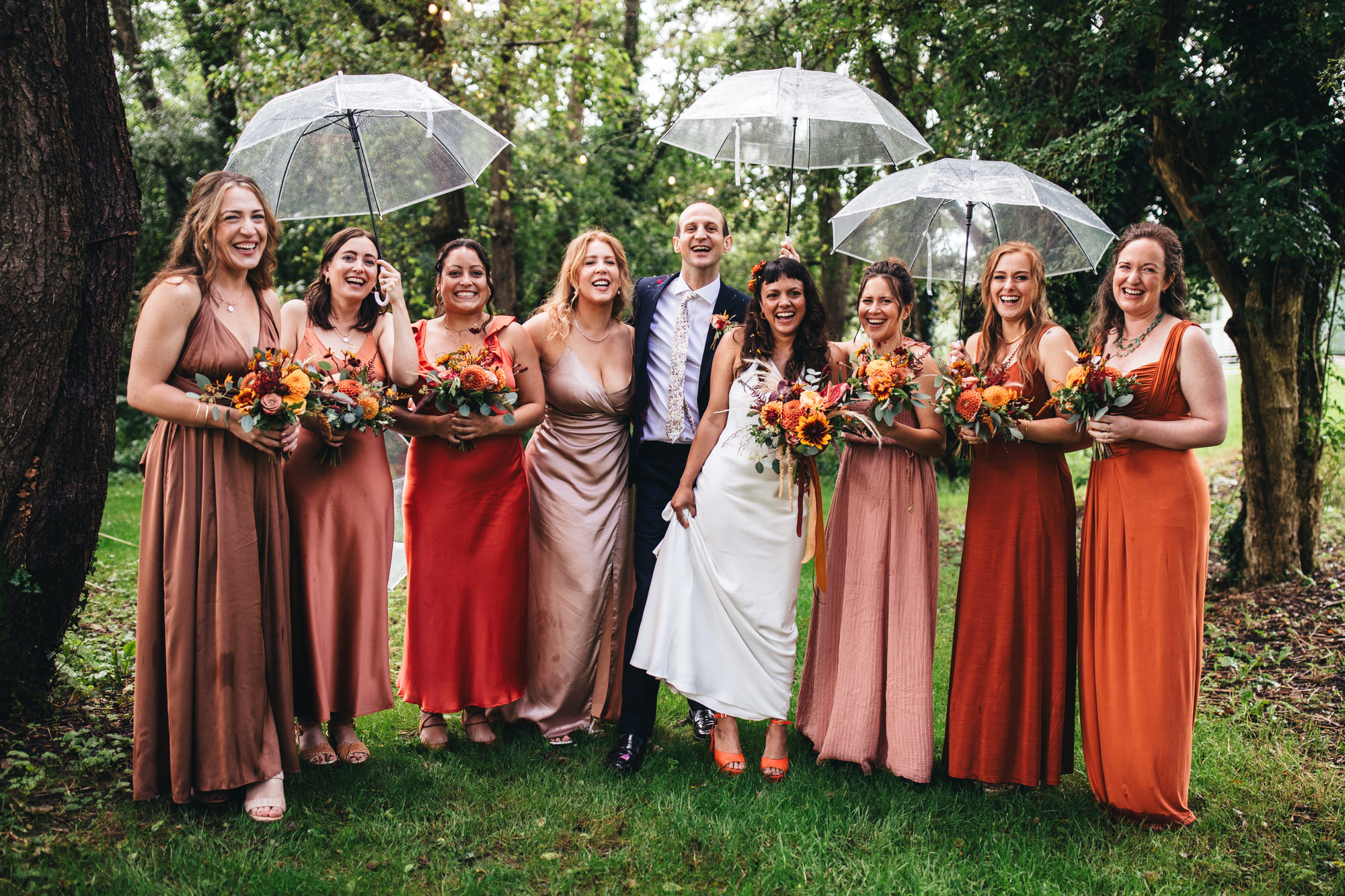 line up of bdie and groom with bridal party, bridesmaids holding up transparent umbrellas
