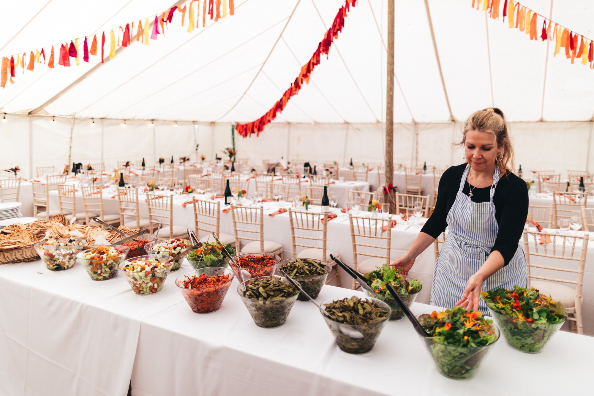 caterer in apron laying table with salads for wedding breakfast in marquee
