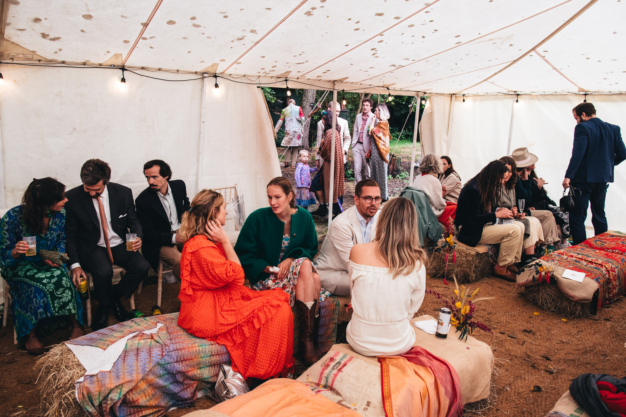 guests sitting on hay bales talking inside marquee tent