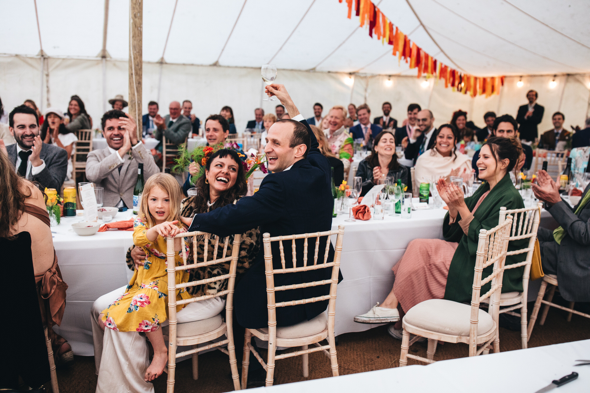 groom toasts with champagne surrounded by smiling clapping guests and bride