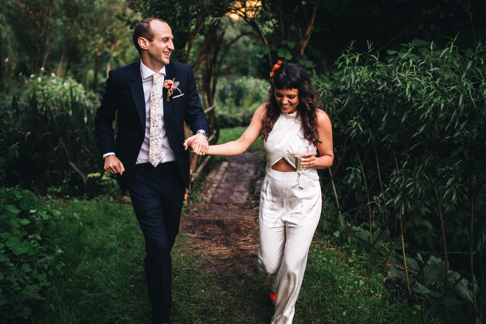 bride and groom walking together through trees, laughing