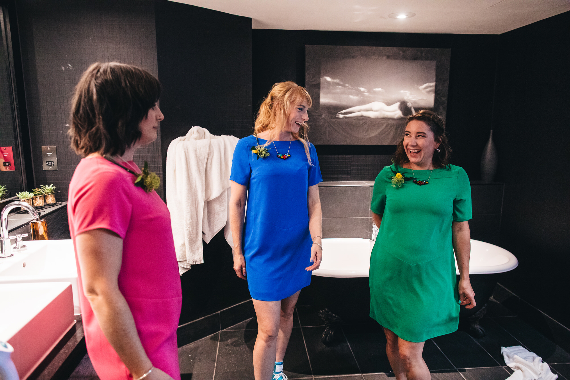 bridesmaids in colourful shift dresses, laughing in bathroom