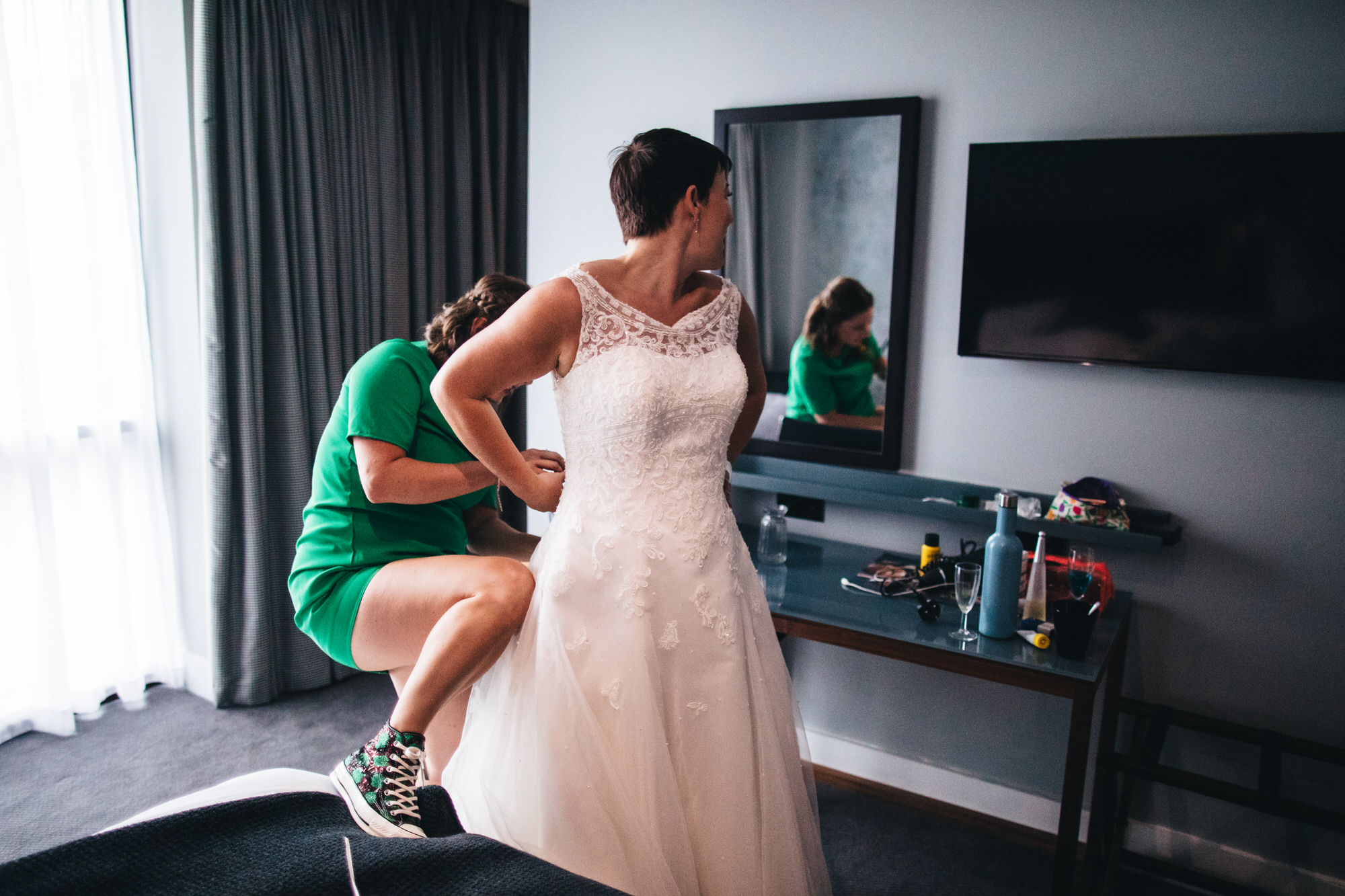 bridesmaid buttoning wedding dress on bride