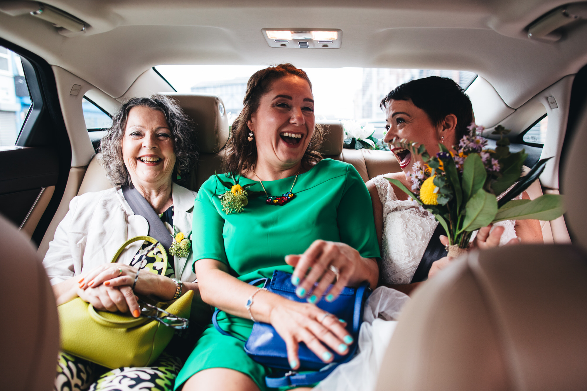 bridesmaid and mother of the bride laughing in car with bride