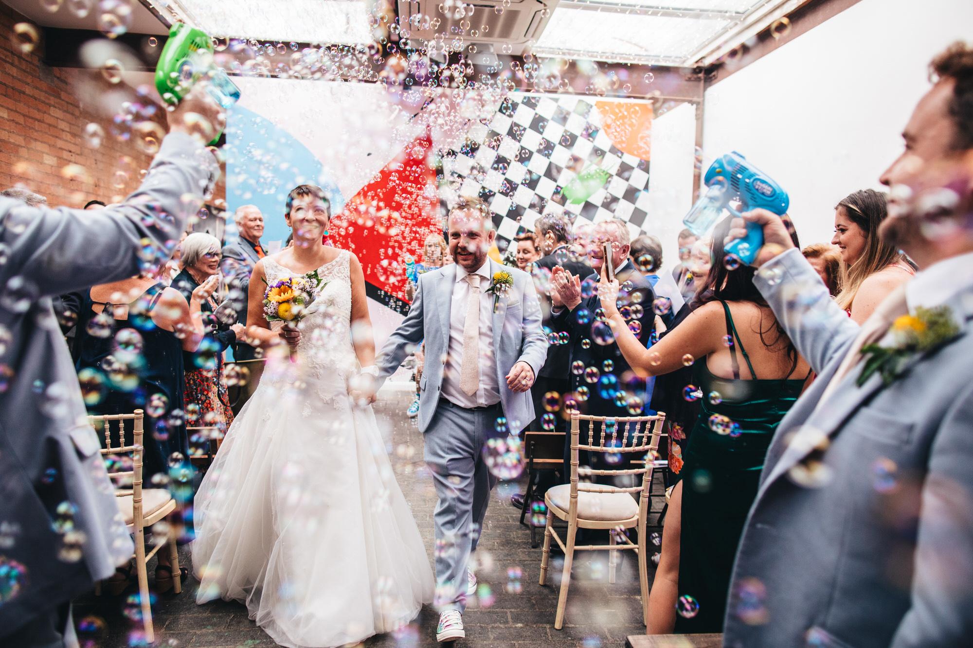 guests blast water gun bubbles at bride and groom walking down aisle together