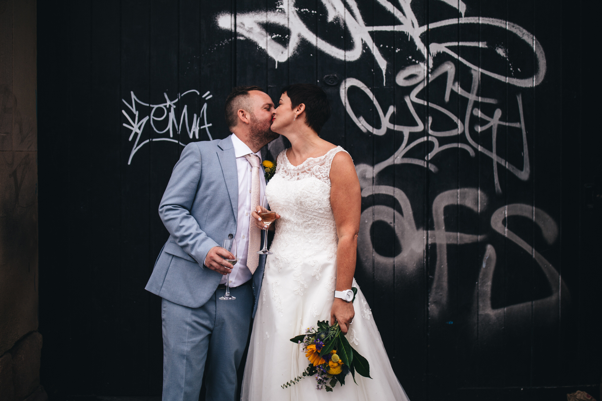 bride and groom kiss before graffiti with champagne