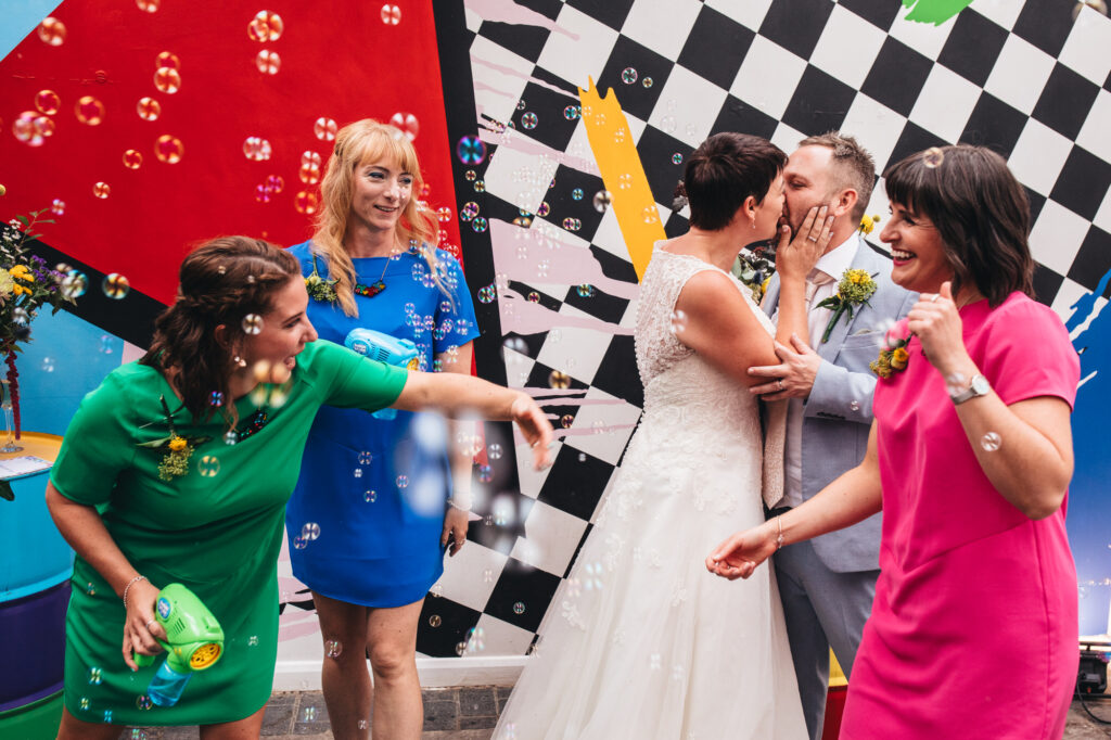 bride kisses groom surrounded by bubbles and bridesmaids