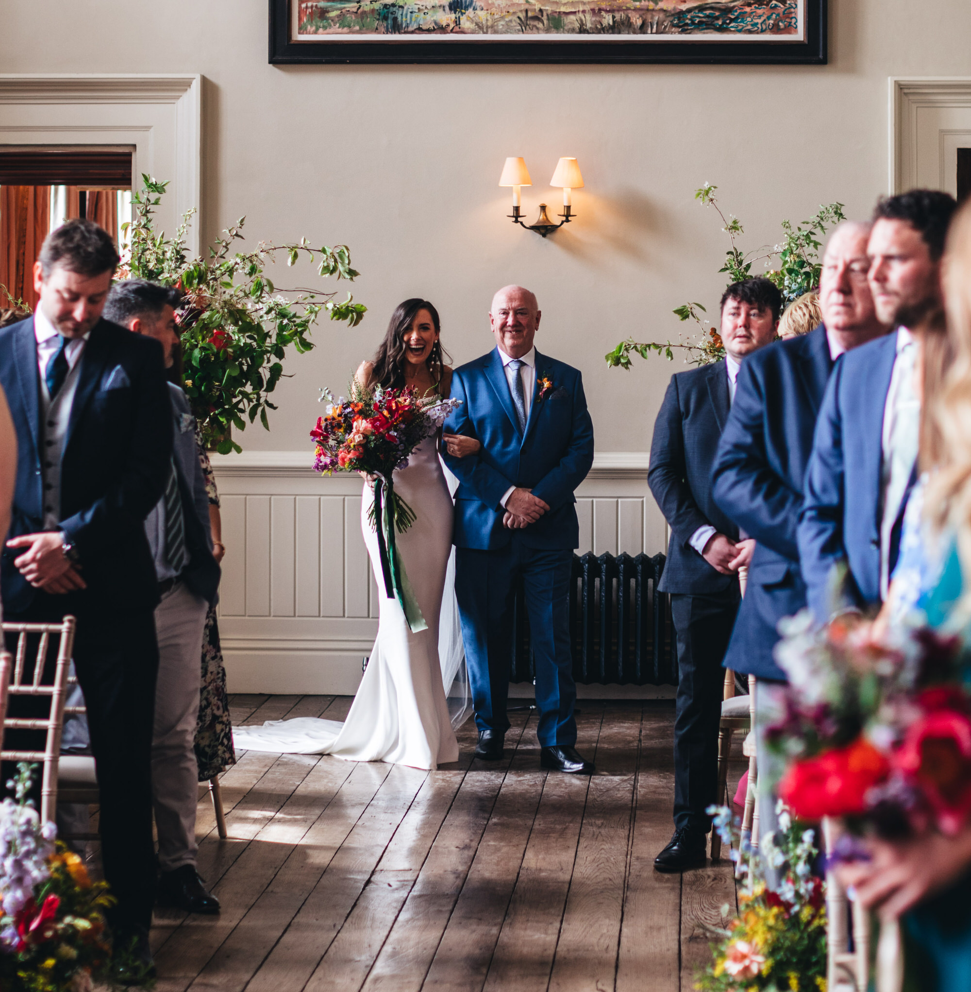 bride laughing with Wren and May bouquet, walking with father down aisle at Elmore Court Hall