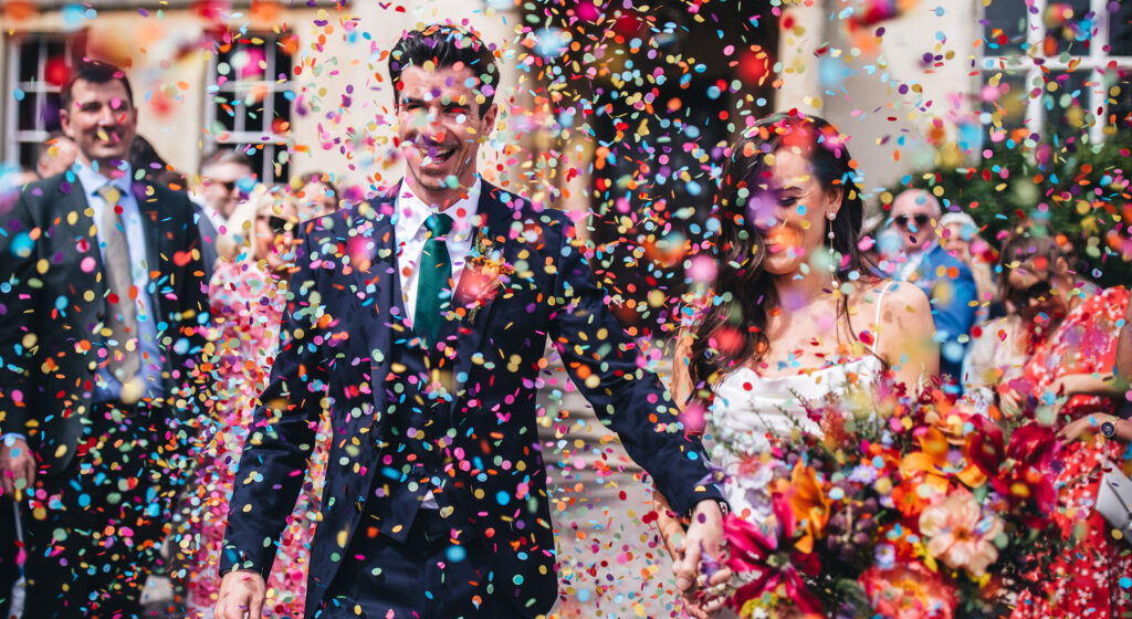 wedding bride and groom walking through colourful paper confetti outside Elmore Court, Elmore Court wedding photography