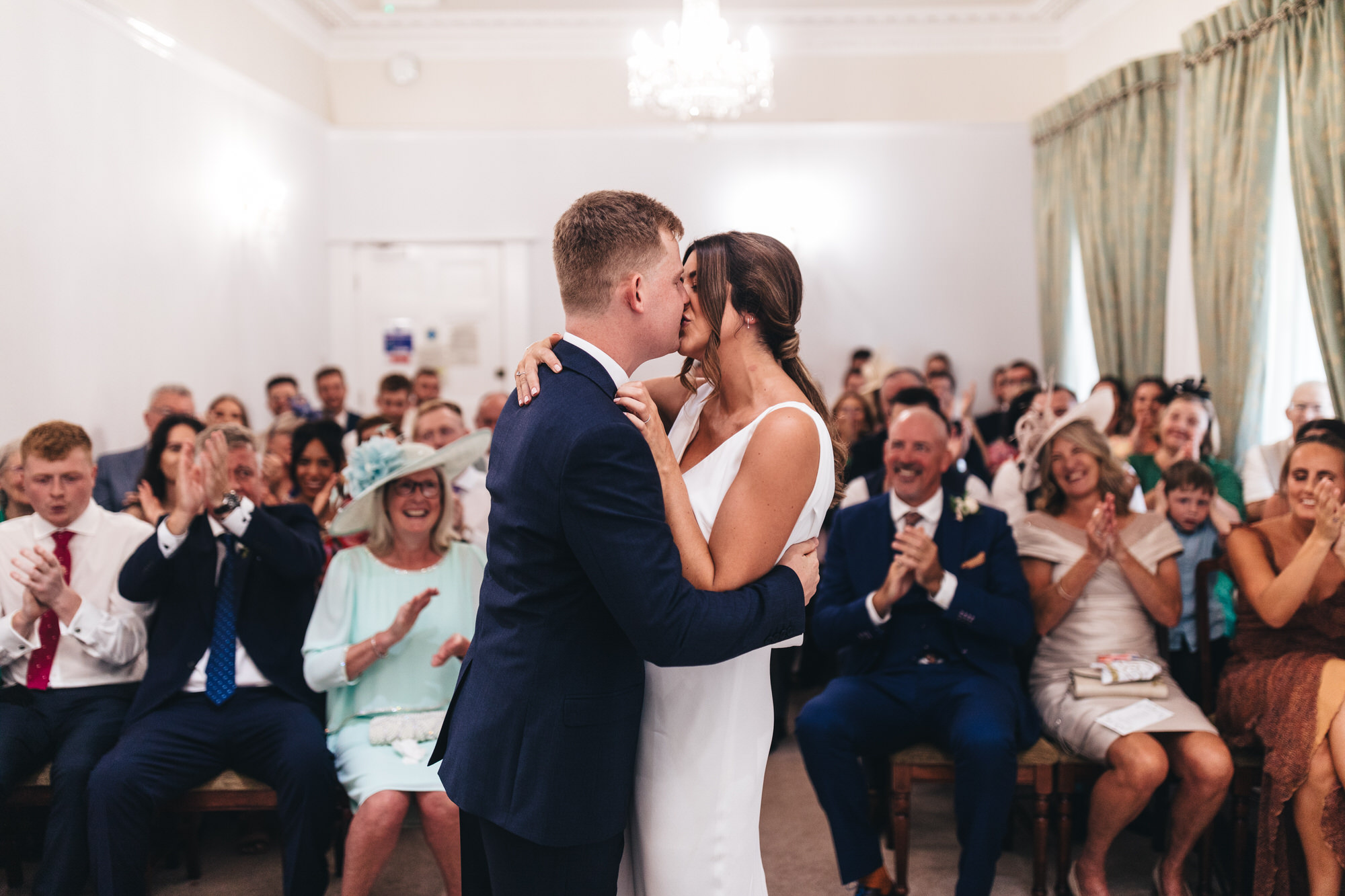 groom and bride kissing at ceremony, guests applaud, clapping
