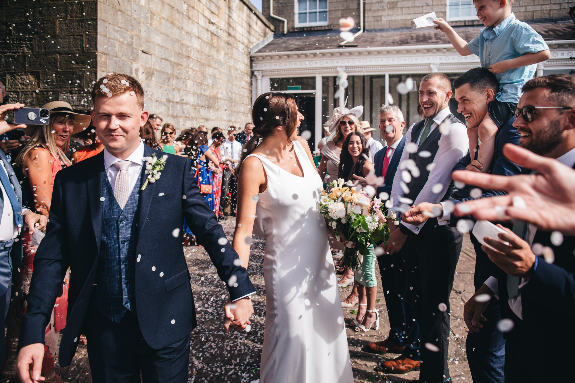 guests throwing confetti at bride and groom in sunshine