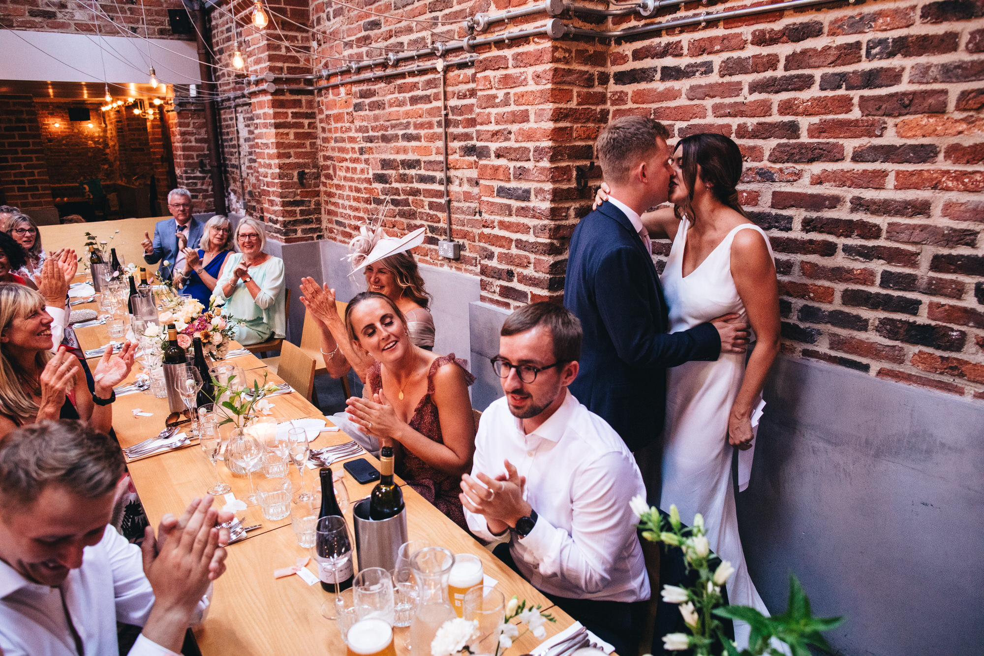 groom kissing bride at wedding reception in front of guests clapping