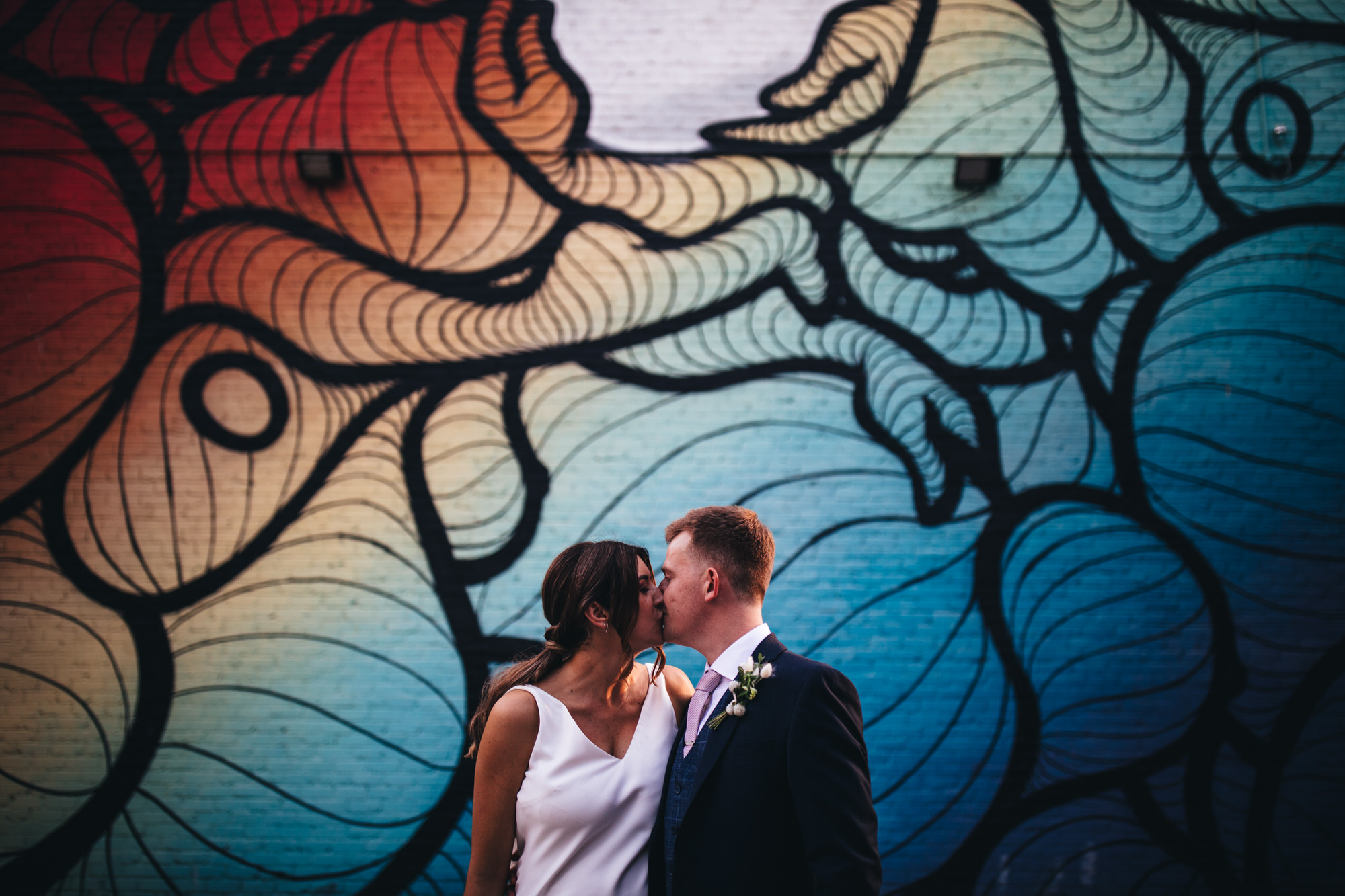 bride and groom kiss before mural
