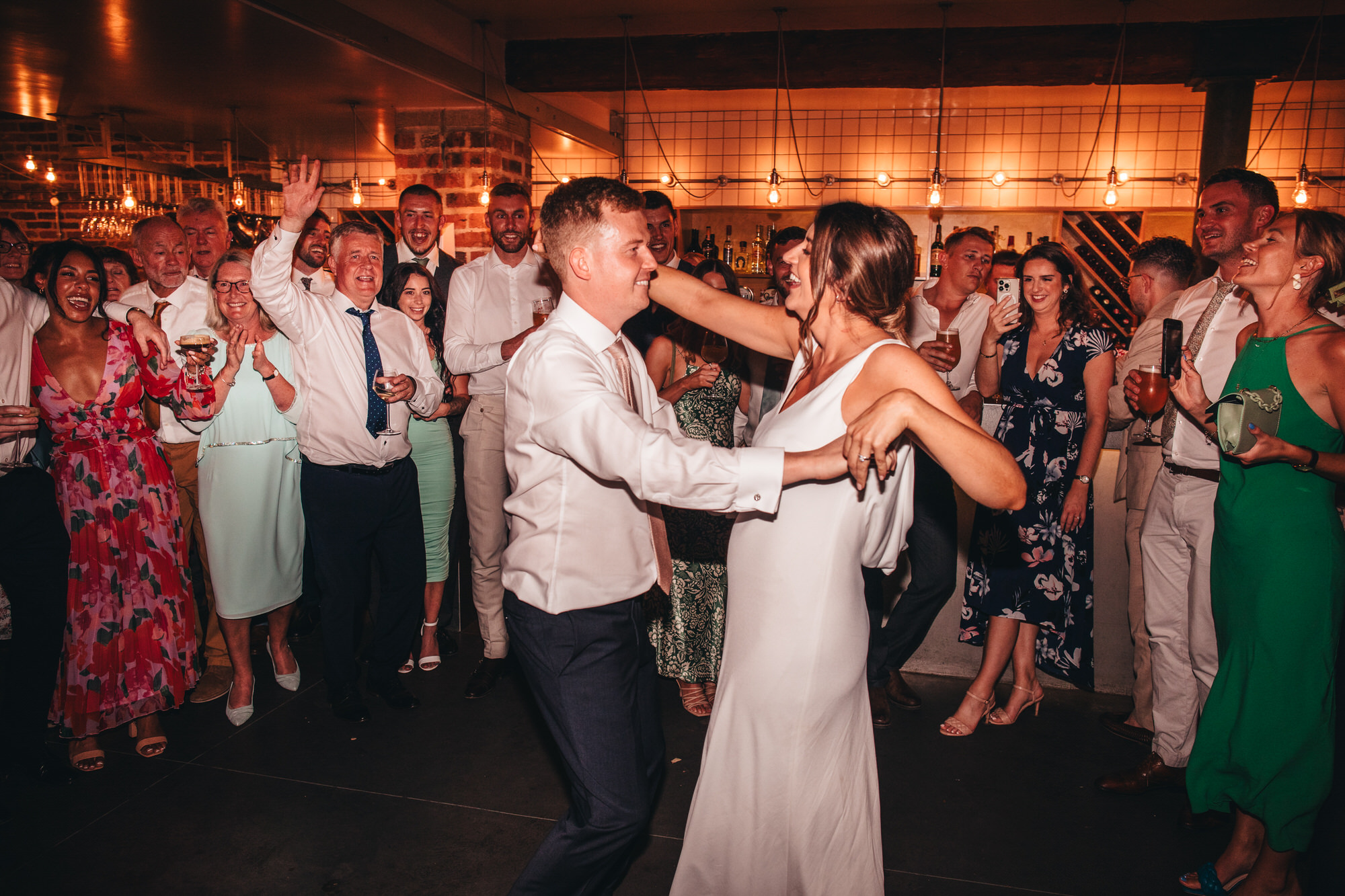 bride and groom dancing together on dancefloor for first dance with crowd of guests watching
