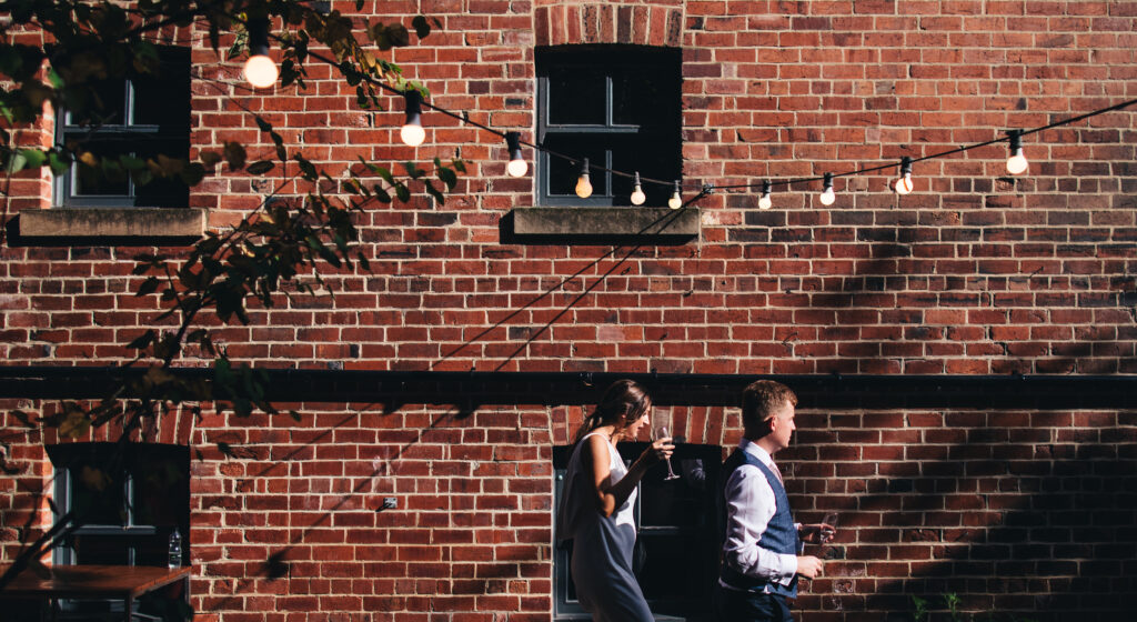 bride and groom walk outside shears yard venue, underneath festoon lights