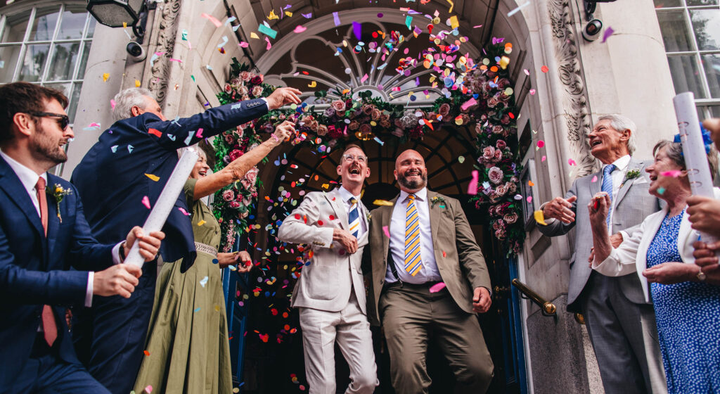 confetti shot, gay wedding, grooms walking outside The Chelsea Old Town Hall, guests throw confetti, London wedding, Chelsea wedding, LGBTQ+ wedding